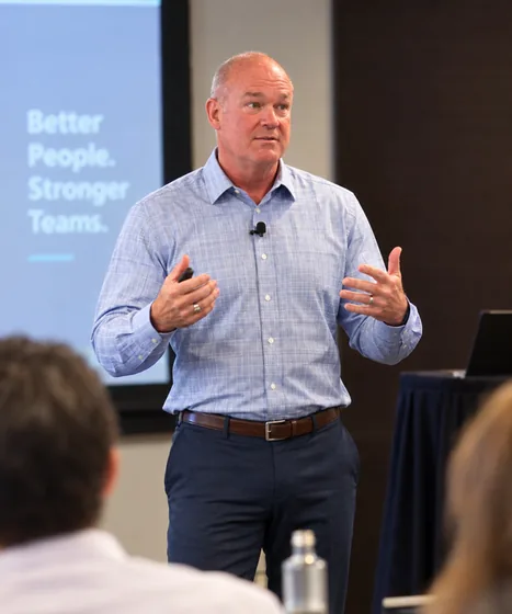 Richard Johnson speaking to an audience in front of a slide that reads Better People, Stronger Teams